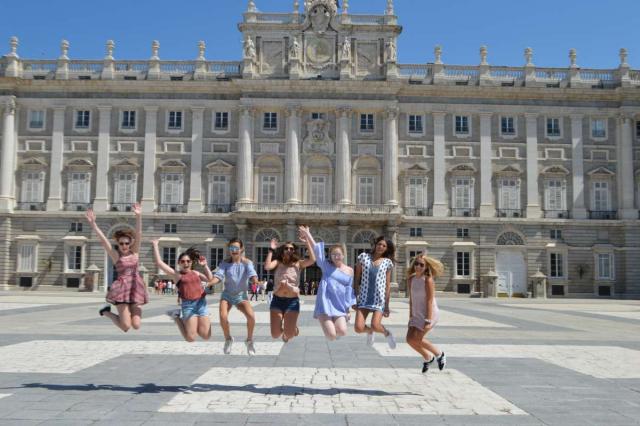 Happy teenage travelers jump in front of Madrid royal palace on summer Spanish language immersion program