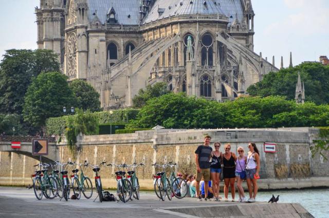 Teenage travelers bike by Notre Dame Cathedral and River Seine on summer youth travel program in Paris