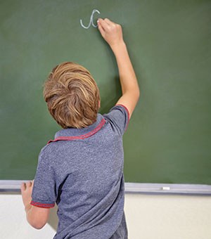 Young boy practicing cursive handwriting on a blackboard