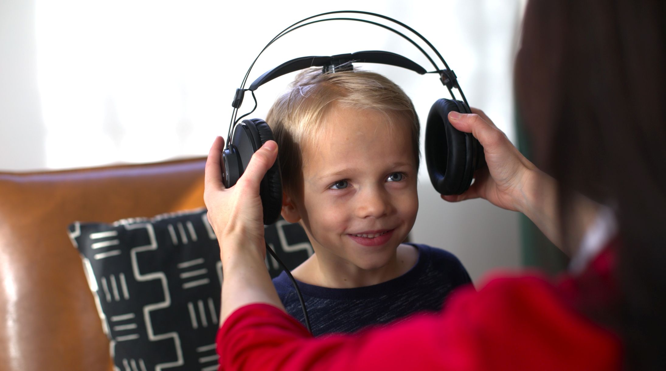 A provider shares a warm moment with a child wearing Waves bone conduction headphones while he colors at a table during a Listening Program session at home