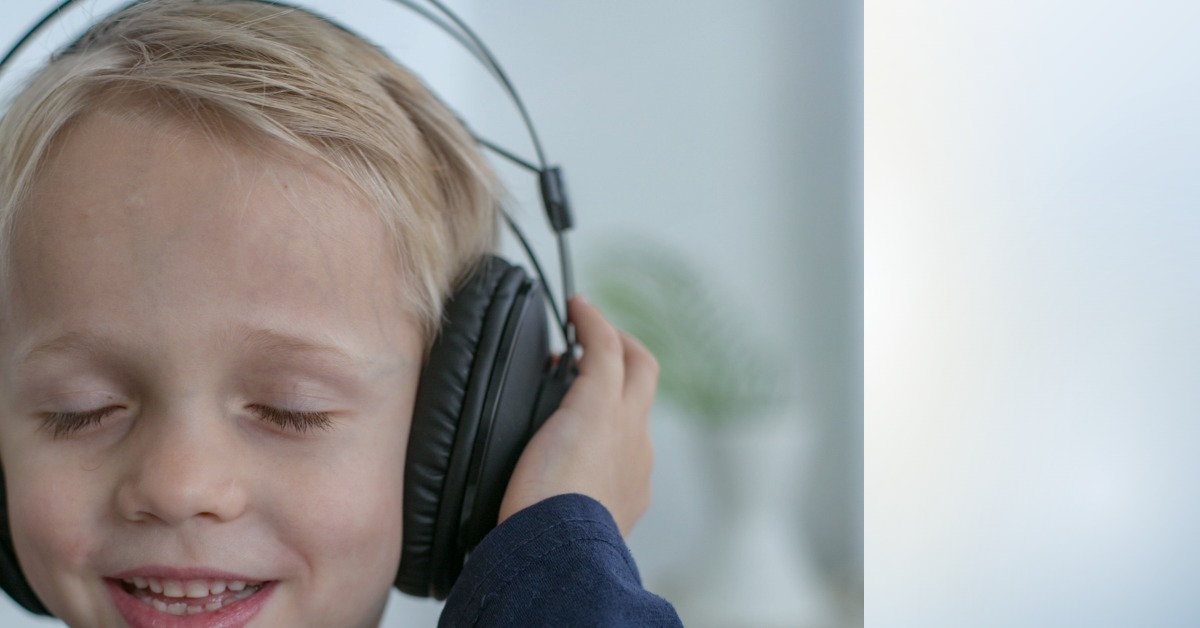A young boy smiling with his eyes closed while wearing headphones, resting calmly during a quiet moment at home.
