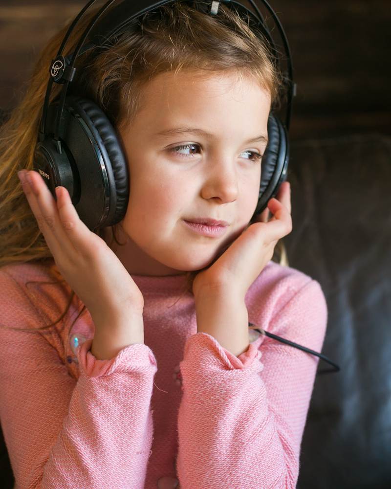 A girl in a pink sweater holds her headphones and listens
