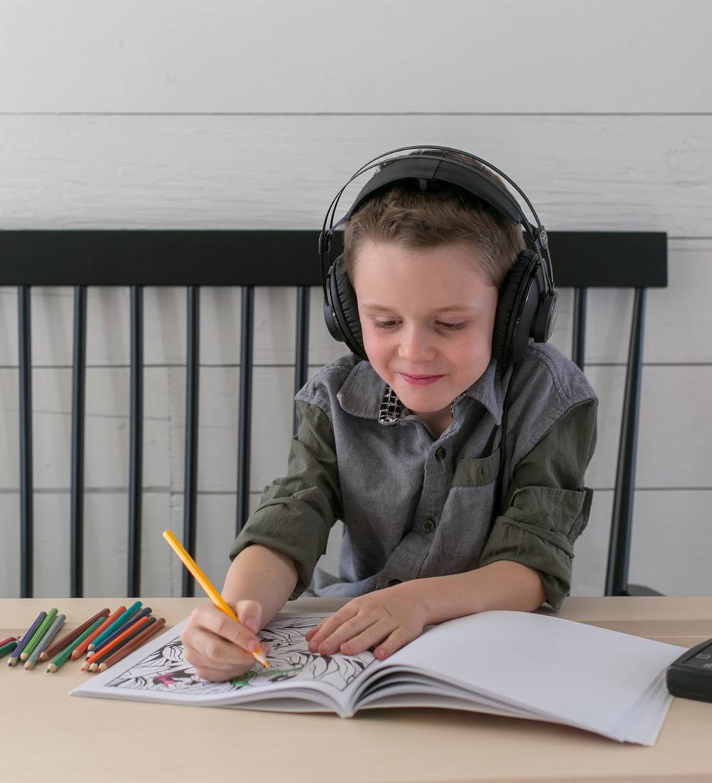 A boy wearing headphones smiles while coloring at a table