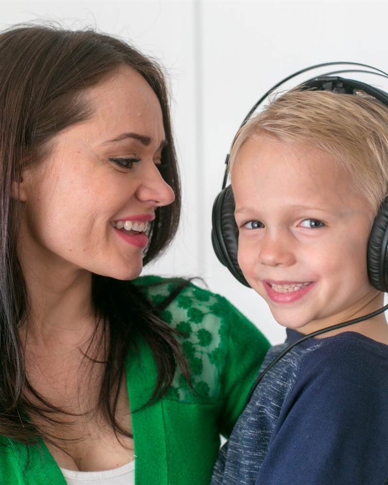 A mother holds her smiling son, who is wearing headphones