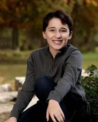 Nicholas smiling, sitting outdoors on a stone wall