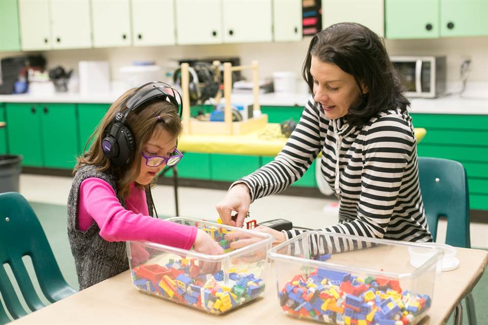 A therapist works with a young girl wearing headphones at a classroom table