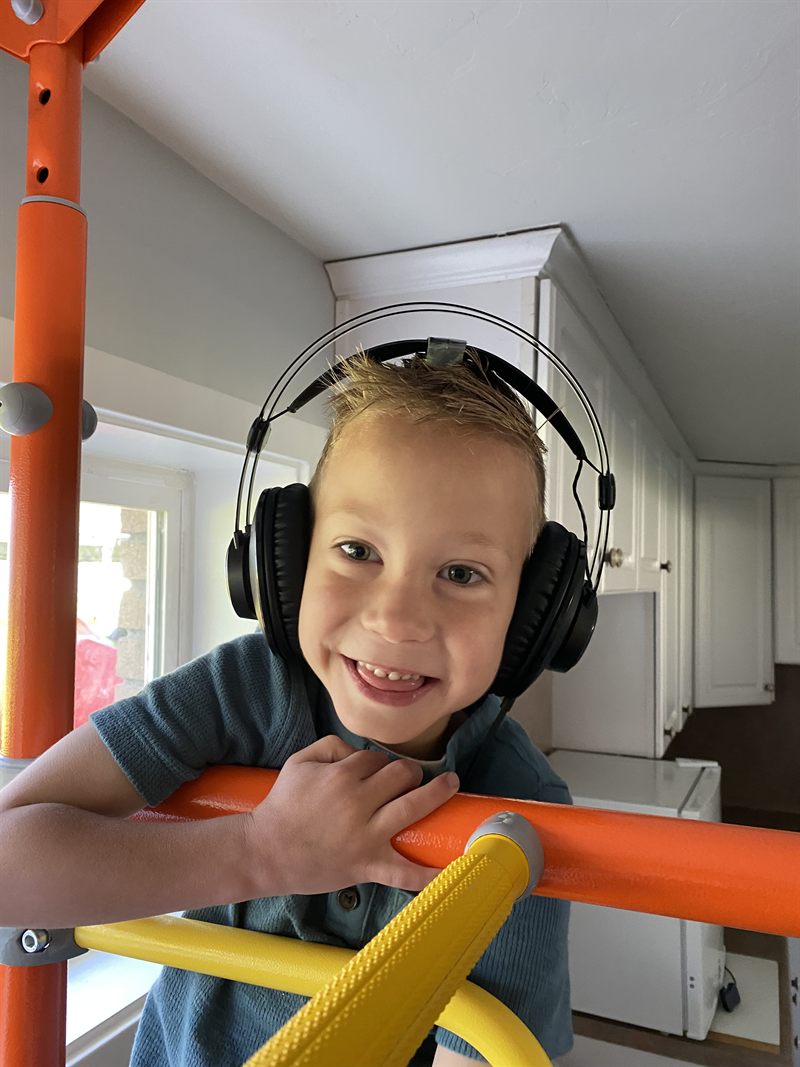 Theo, smiling, wearing Waves headphones as he leans on an orange climbing frame