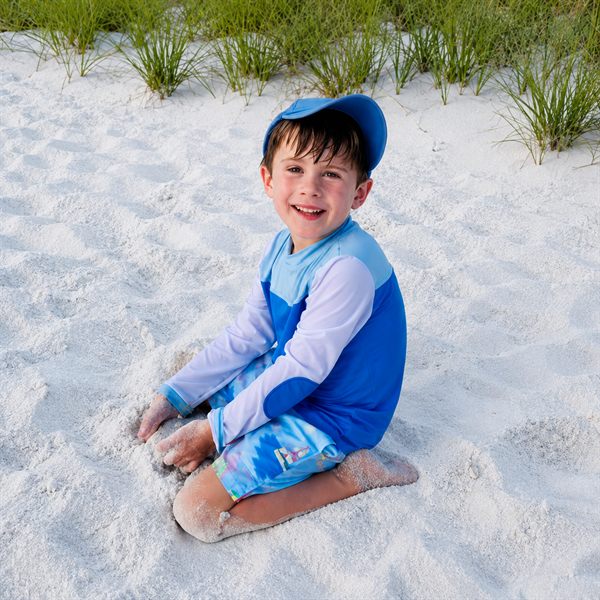 Christopher, smiling, sitting in white sand at the beach