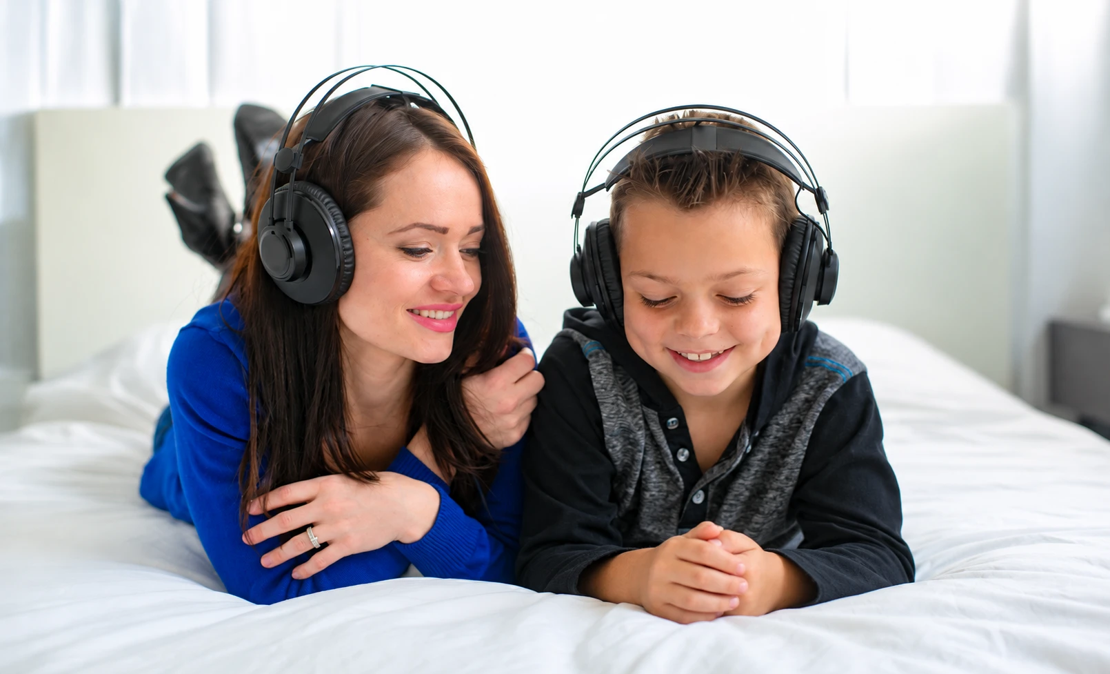 A woman and a boy smiling as they listen to music with headphones at home